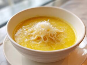 Close-up of a bowl of vibrant yellow sweet corn soup topped with fine white shreds.