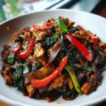 A close-up of a bowl filled with stir-fried Thai drunken noodles recipe chicken, wide dark noodles, red peppers, and basil.