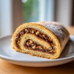 Close-up of a slice of Valerie Bertinelli Italian Nut Roll Cookies showing rich nut filling and powdered sugar.