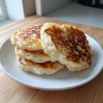 A stack of four golden-brown vegan sourdough discard pancakes served on a white plate.