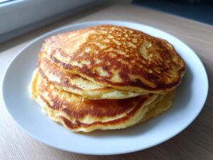 A stack of three fluffy vegan sourdough discard pancakes with golden-brown, textured tops served on a white plate.