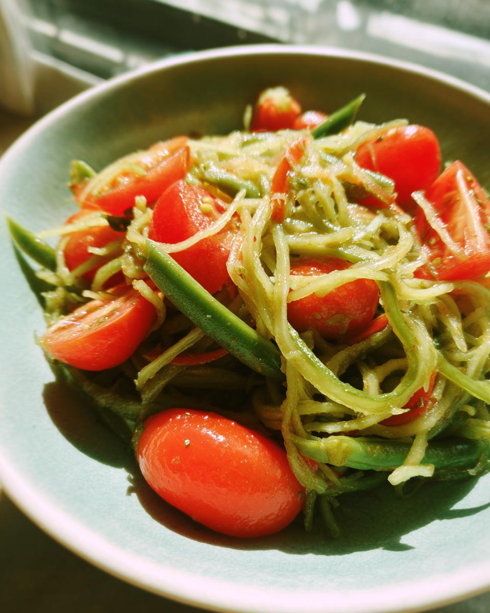 Close-up of a bowl of fresh green papaya salad mixed with bright red cherry tomatoes and green beans.