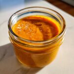 Close-up of thick, vibrant orange papaya salad dressing blended smooth in a small glass jar.