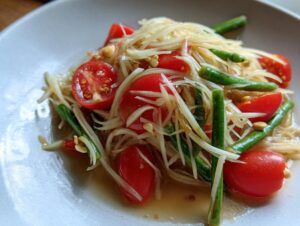 Close-up of a refreshing raw papaya salad featuring shredded green papaya, bright red cherry tomatoes, and green beans.