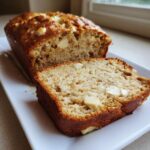 A close-up of a slice of moist white chocolate banana bread next to the loaf.