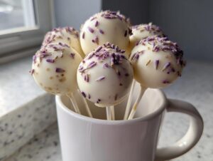 Several white chocolate lavender cake pops topped with dried lavender buds, displayed upright in a white mug.