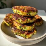 A stack of five golden-brown air fryer zucchini patties served in a rustic bowl.