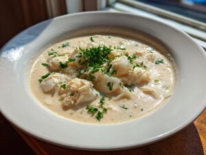 A close-up of a creamy bowl of amazing crab soup topped with large chunks of white crab meat and fresh parsley.