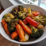 A close-up of perfectly seasoned roasted vegetables, including broccoli, carrots, and red peppers, served in a white bowl.