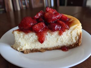 A perfect slice of creamy strawberry cheesecake resting on a white plate, topped with glistening strawberry compote.