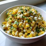 Close-up of a white bowl filled with vibrant yellow street corn salad topped with crumbled white cheese and fresh cilantro.