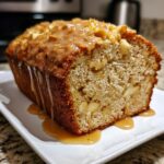 A close-up of a freshly baked apple amaretto cake loaf, drizzled with a thick caramel glaze.