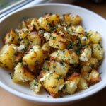 Close-up of golden brown baked feta potatoes mixed with crumbled feta cheese and fresh parsley in a white serving bowl.