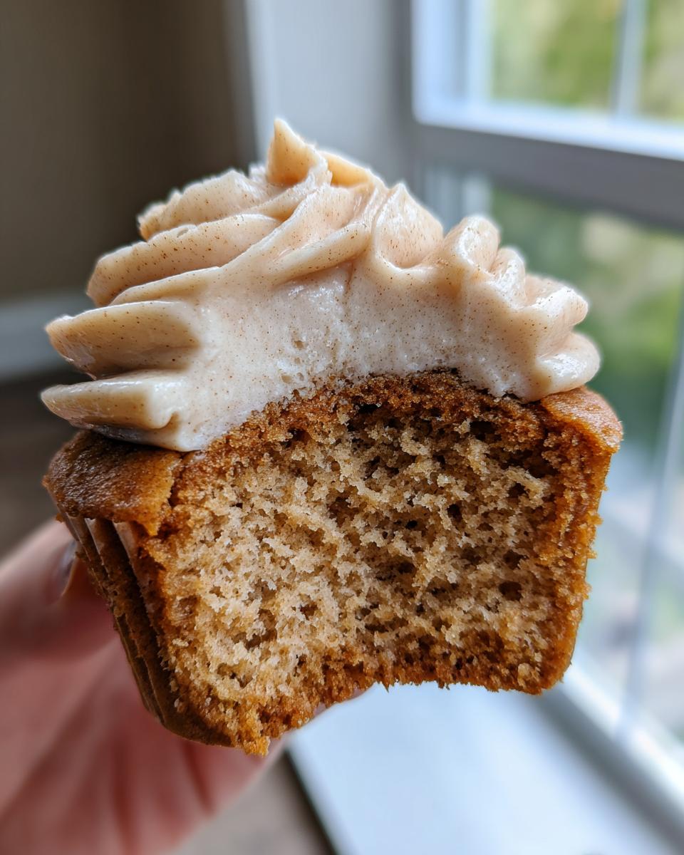 Close-up of a banana cupcake with cinnamon frosting, showing the moist crumb texture inside.
