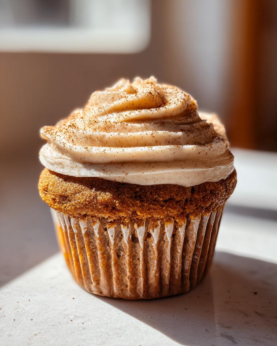 A single, perfectly baked banana cupcake topped with swirled cinnamon frosting and a dusting of spice.