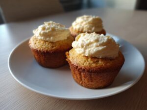 Three freshly baked banana cupcakes from box cake hack topped with thick cream cheese frosting on a white plate.