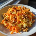 A bright, close-up serving of carrot apple walnut salad featuring shredded carrots, apple chunks, and whole walnuts.