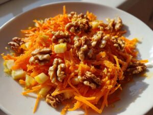 Close-up of a bright carrot apple walnut salad featuring shredded carrots, diced apples, and whole walnuts on a white plate.