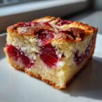 Close-up of a square slice of cherry dump cake with cream cheese, showing bright red cherries baked into a golden cake.