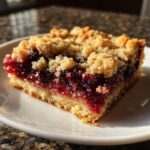 Close-up of a square slice of cherry dump cake with pie filling showing a buttery crust and crumb topping.