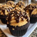 Close-up of a rich chocolate peanut butter cupcakes topped with peanut butter frosting, chocolate ganache drizzle, and chopped peanuts.