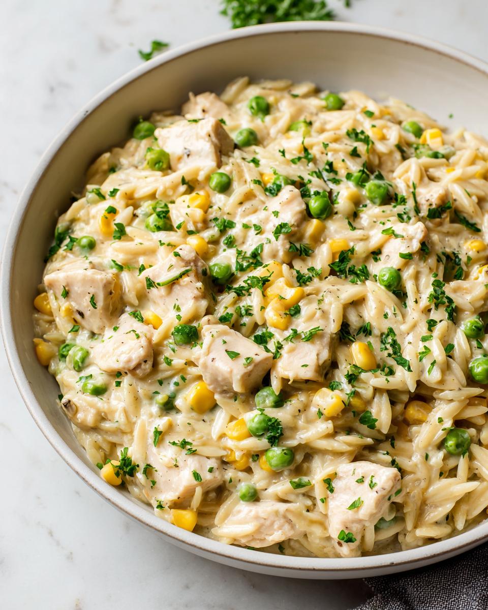 Close-up of creamy chicken pot pie orzo with chunks of chicken, peas, and corn, topped with parsley.