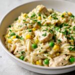 Close-up of creamy chicken pot pie orzo mixed with peas and corn, topped with fresh parsley.