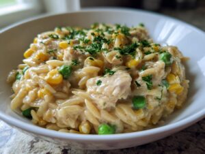 A close-up of creamy chicken pot pie orzo mixed with corn and peas, topped with fresh parsley.