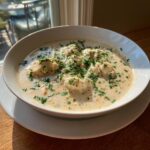 A close-up of a creamy, rich bowl of crab soup generously topped with fresh chopped parsley.