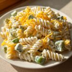 Close-up of creamy dill pickle pasta salad made with rotini pasta, chunks of pickle, and topped with shredded cheddar cheese.