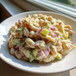 A close-up of a creamy dill pickle white bean salad featuring white beans, diced pickles, red onions, and fresh dill in a white bowl.