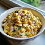 Close-up of a creamy vegan street corn salad featuring yellow corn, red onion, and cilantro in a white bowl.