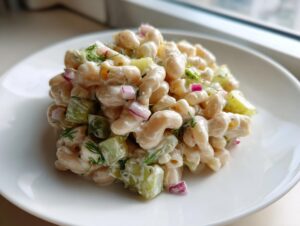 Close-up of a creamy dill pickle white bean salad made with elbow macaroni, pickles, and red onion on a white plate.