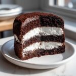 A cross-section slice of a layered ding dong cake featuring dark chocolate cake and thick white cream filling.