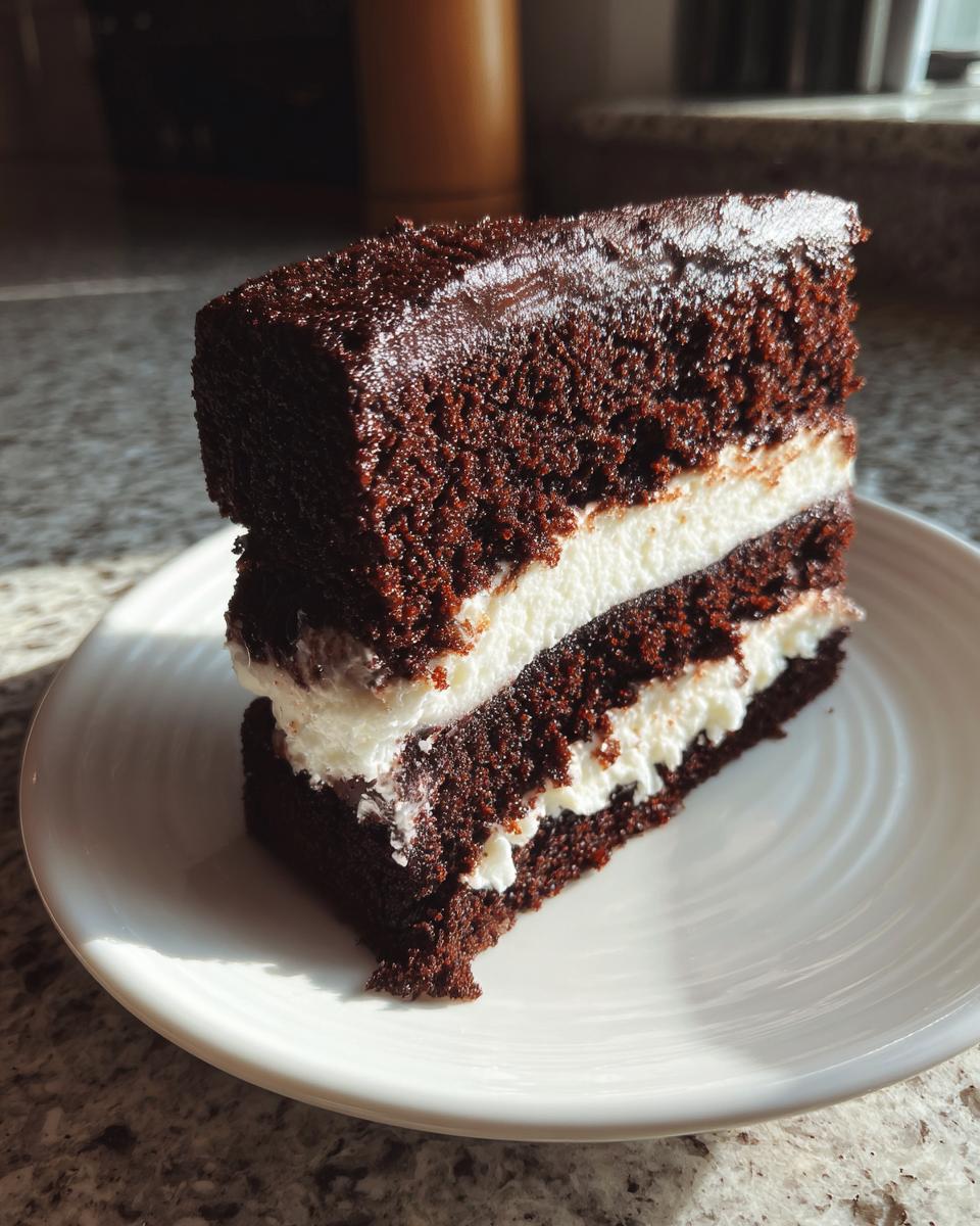 A decadent slice of ding dong cake showing two layers of dark chocolate cake separated by thick white cream filling.