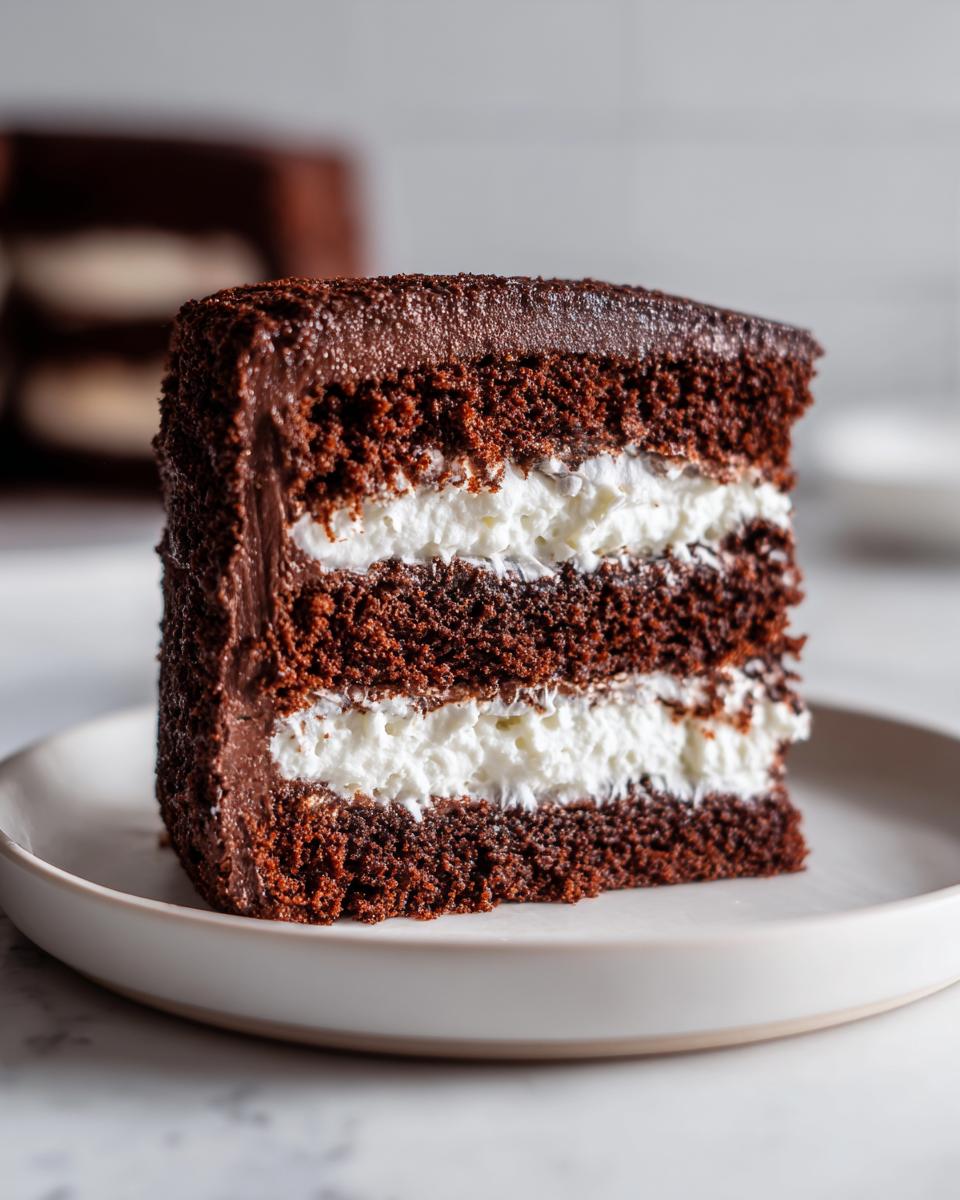 Close-up of a decadent slice of Ding Dong Cake showing three layers of dark chocolate cake and two layers of white cream filling.