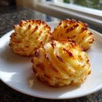 Three golden-brown duchess potatoes plating mounds with piped ridges sitting on a white plate.