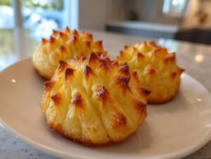 Three perfectly piped and browned duchess potatoes plating examples on a white dish.