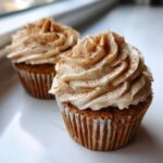 Close-up of two fluffy banana cupcakes topped with swirled cream frosting dusted heavily with cinnamon.