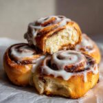 A close-up stack of four gooey, freshly baked cinnamon rolls recipe treats covered in thick white icing.