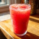 Close-up of a tall glass filled with bright red, icy frozen strawberry lemonade condensation on the glass.