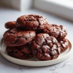 A tempting stack of rich, dark chocolate brownie mix cookies piled high on a light-colored plate.