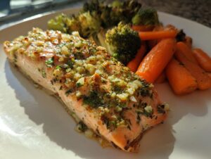A perfectly cooked fillet of garlic herb salmon topped with minced garlic and herbs, served next to roasted carrots and broccoli.