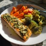 A perfectly cooked fillet of garlic herb salmon with roasted broccoli and carrots on a white plate.