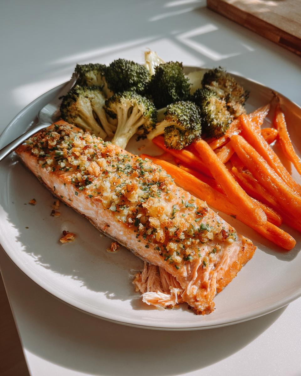 Flaky garlic herb salmon served alongside roasted broccoli florets and bright orange carrot sticks on a light plate.