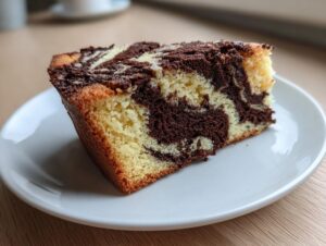 A close-up of a moist slice of german marble cake showing distinct vanilla and chocolate swirls on a white plate.