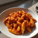 A close-up of a white bowl filled with homemade gluten-free cavatelli pasta coated in a vibrant red sauce.