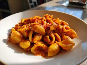 Close-up of a serving of gluten-free cavatelli pasta coated in a rich, chunky red tomato sauce on a white plate.