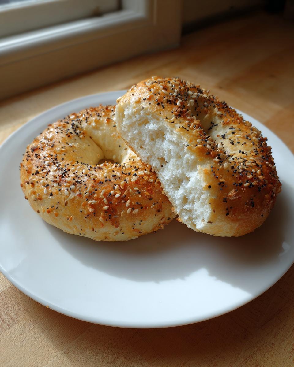 A greek yogurt protein bagel, topped with everything seasoning, cut in half to show the fluffy white interior on a white plate.
