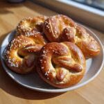 A plate piled high with golden brown, freshly baked high-protein high-fiber pretzels sprinkled with coarse salt.